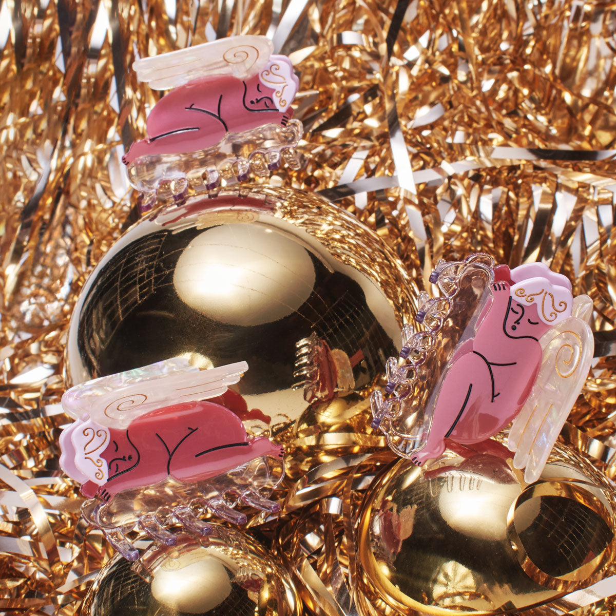 Group of Cherub Hair Claw in Pink by Winona Irene on sparkling gold tinstle background. Part of the Holiday Collection.